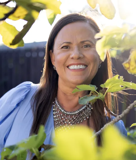 Isa Herrera outdoors in natural light wearing a silver necklace, green foliage behind her.