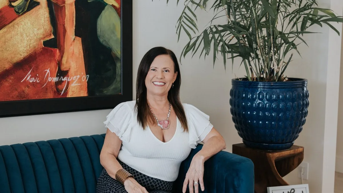 Isa Herrera in a white top on a teal sofa beside a framed painting.