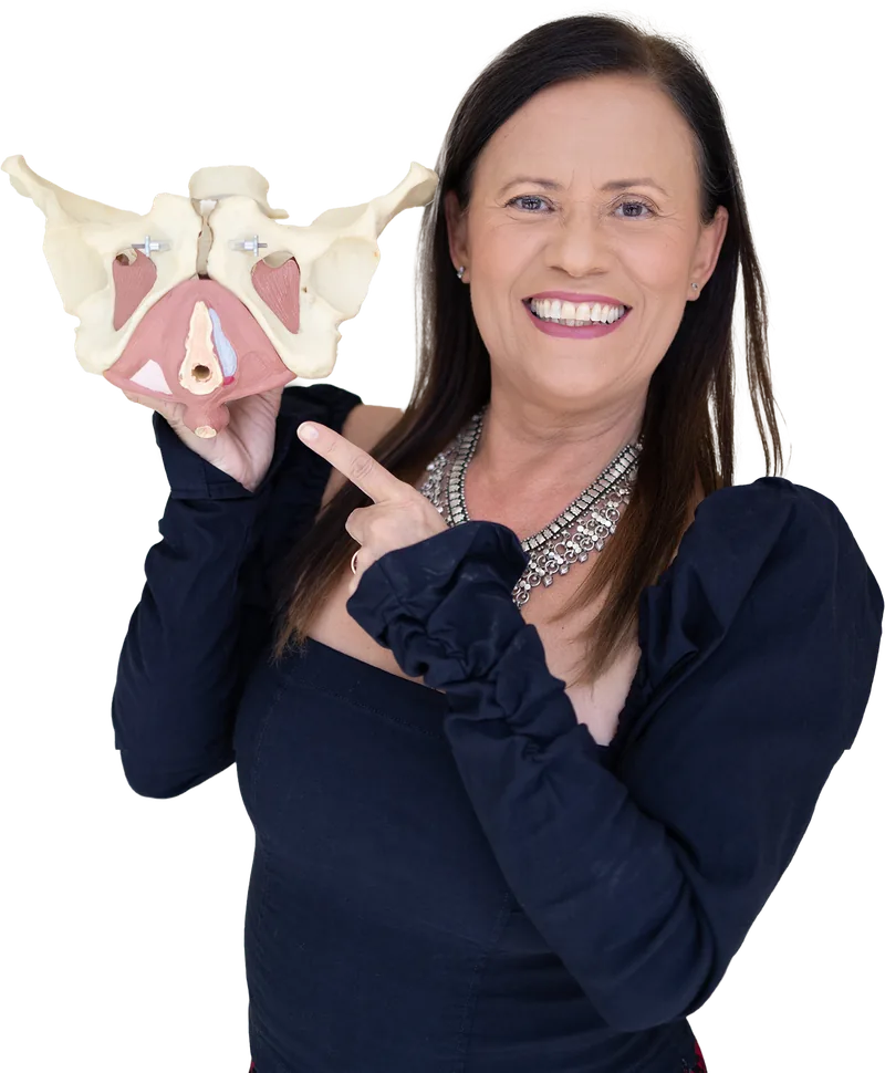 Isa Herrera smiling and pointing at an anatomical pelvis model with the muscle layer in pink.